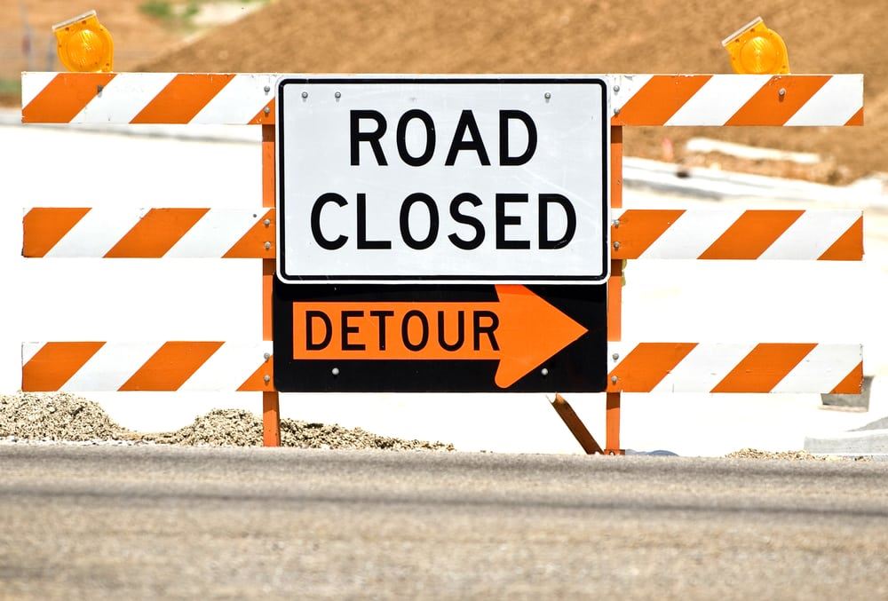 Road Closed sign hanging on a warning barricade