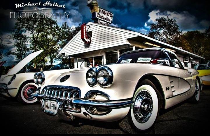 Close up of old shiney white car with lots of sparkly chrome in front of old time gas station